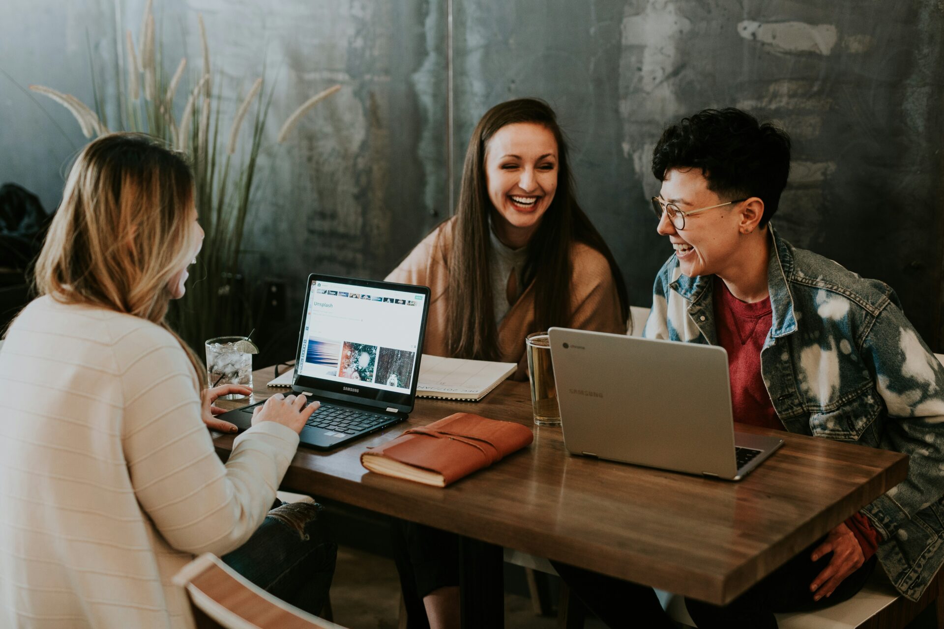 three people sitting in front of a table in an atworld coworking space and laughing together