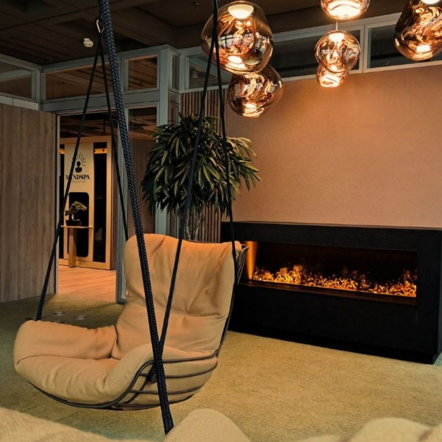 Modern lounge and reception area featuring a hanging chair, warmly lit fireplace, decorative glass pendant lights, and natural wood and beige tones creating a cozy atmosphere.1080X1080